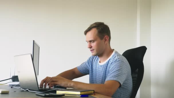 Een man zit achter een bureau thuis, thuis werken, computer en laptop. — Stockvideo
