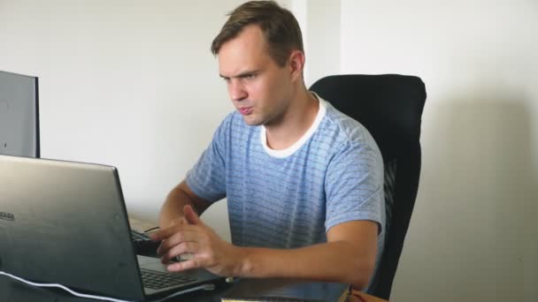 Um homem sentado em uma mesa em casa, trabalhando em casa computador e laptop . — Vídeo de Stock