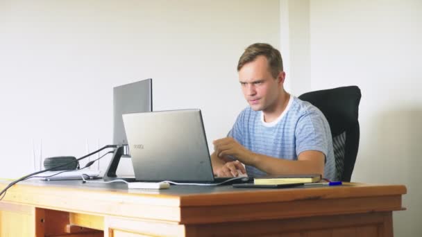 Um homem sentado em uma mesa em casa, trabalhando em casa computador e laptop . — Vídeo de Stock