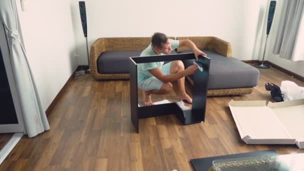 Ein junger Mann sammelt selbstständig Möbel im Wohnzimmer seines Hauses. Ein Mann sammelt einen Computertisch. — Stockvideo