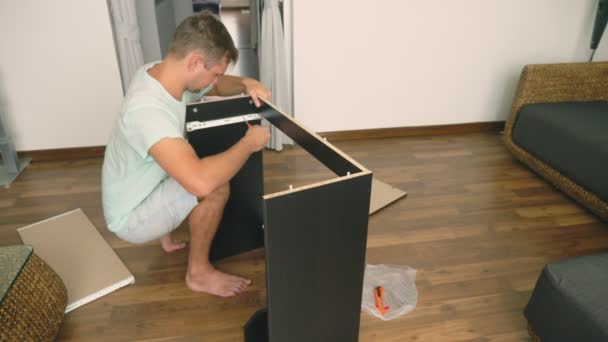 Молодой человек самостоятельно собирает мебель в гостиной своего дома. Мужчина собирает компьютерный стол . — стоковое видео