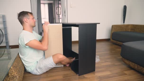 A young man independently collects furniture in the living room of his house. A man collects a computer desk. — Stock Video