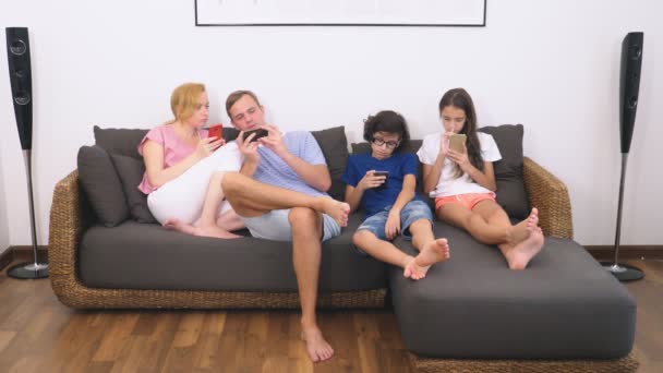 Keluarga yang menawan, ibu, ayah, anak perempuan dan anak menonton TV di ruang tamu bersama-sama, semua orang melihat ke dalam teleponnya — Stok Video