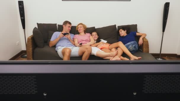 Charmiga familj, Mamma, Pappa, dotter och son tittar på Tv i vardagsrummet tillsammans — Stockvideo