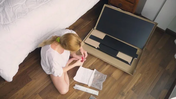 Monteren van meubels thuis, assembleert een huisvrouw een computerbureau met behulp van handgereedschap. — Stockfoto