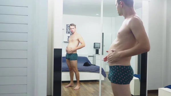 Jeune homme vérifiant ses muscles devant un miroir dans la chambre — Photo