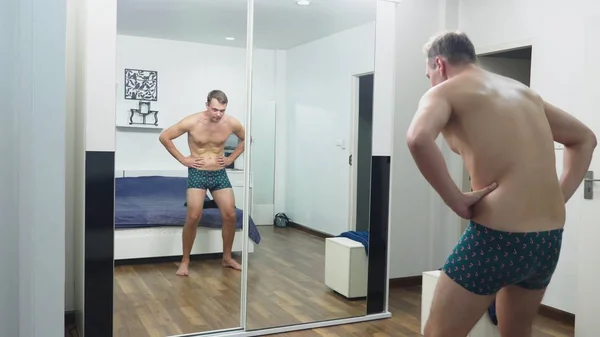 Νεαρός άνδρας, ελέγχοντας τους μυς του μπροστά από έναν καθρέφτη στο υπνοδωμάτιο — Φωτογραφία Αρχείου