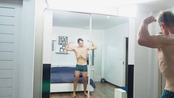 Joven comprobando sus músculos delante de un espejo en el dormitorio — Foto de Stock