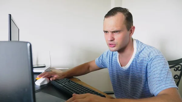 A man sitting at a desk at home, working at home computer and laptop. — Stock Photo, Image