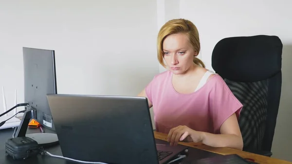 Bela jovem mulher trabalhando em um laptop e computador enquanto sentado em uma mesa . — Fotografia de Stock