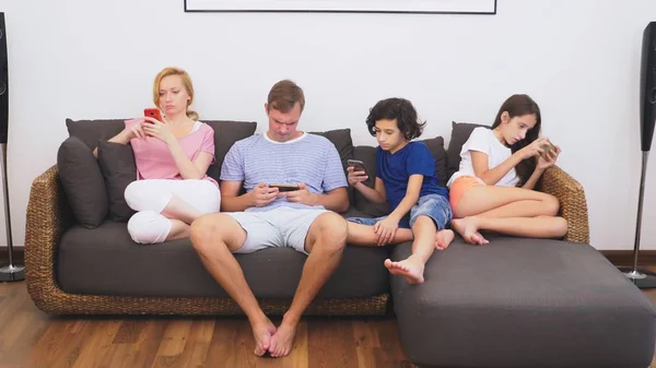 Charmante famille, maman, papa, fille et fils regardent la télévision dans le salon ensemble, tout le monde regarde dans son téléphone — Photo