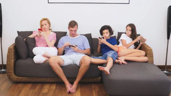 Familia encantadora, mamá, papá, hija e hijo están viendo la televisión en la sala de estar juntos, todo el mundo está mirando en su teléfono — Foto de Stock