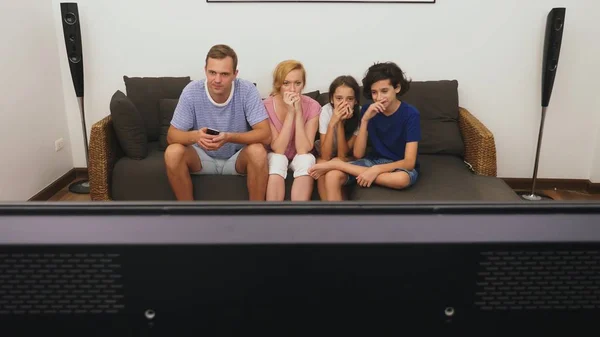 Очаровательная семья, мама, папа, дочь и сын смотрят телевизор в гостиной вместе — стоковое фото