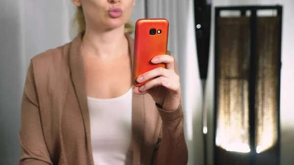 여성 flirts 그녀의 smartphone에서 비디오 통신에 대 한 얘기. 여자는 스마트폰을 사용 하 여 화상 통화 하는 동안 온라인 키스를 보냅니다.. — 스톡 사진