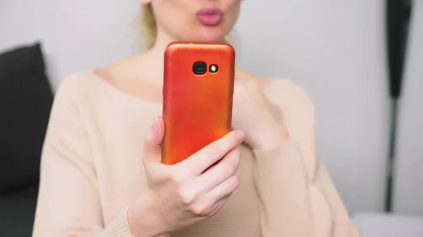 woman flirts talking on video communication from her smartphone. A woman sends a kiss online during a video call using a smartphone.