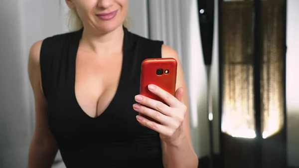 Bella ragazza utilizzare uno smartphone cellulare mentre seduto in soggiorno la sera. Felice sorridente giovane donna che chiacchiera su internet a casa . — Foto Stock