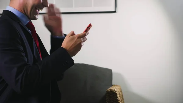 Beautiful gay use a cellular smartphone while sitting in the living room in the evening. Happy smiling young man chatting on the internet at home. — Stock Photo, Image