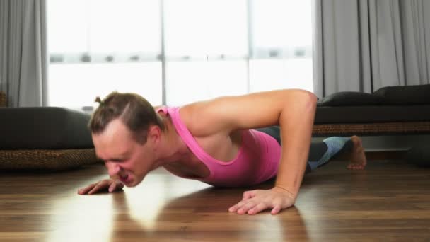 Playful handsome guy in a pink t-shirt engaged in fitness, in the living room of his house. — Stock Video