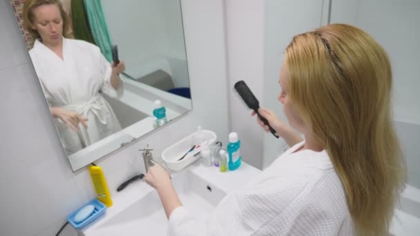 Salud del cabello, concepto de pérdida de cabello. Mujer peinando su cabello rubio seco dañado en el baño — Vídeos de Stock