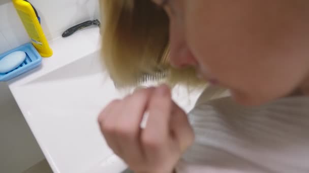 Haar gezondheid, haar verlies concept. Vrouw kammen van haar blond beschadigd droge haren in de badkamer — Stockvideo