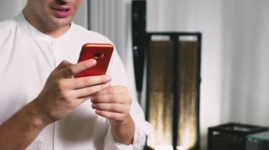 Güzel eşcinsel akşamları oturma odasında otururken hücresel bir akıllı telefon kullanın. Mutlu gülümseyen genç adam evde internet sohbet.