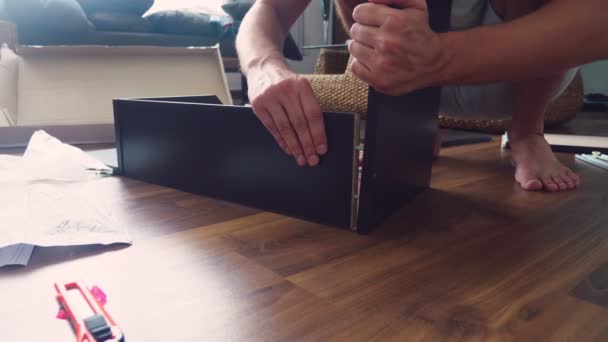 A young man independently collects furniture in the living room of his house. A man collects a computer desk. — Stock Video