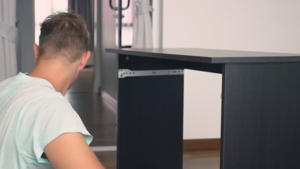 Egy fiatal férfi önállóan gyűjt bútor a nappaliban a házból. Az ember gyűjt a számítógép asztal. — Stock videók