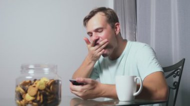 Aç üzgün adam geceleri bir masada oturma odasında oturur, o bir karaciğer yiyor ve onun smartphone kullanır