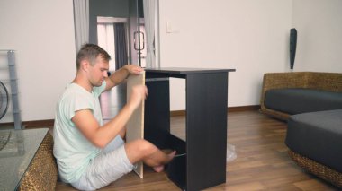 Genç bir adam bağımsız olarak mobilya evinin oturma odasında toplar. Bir adam bilgisayar masası toplar.