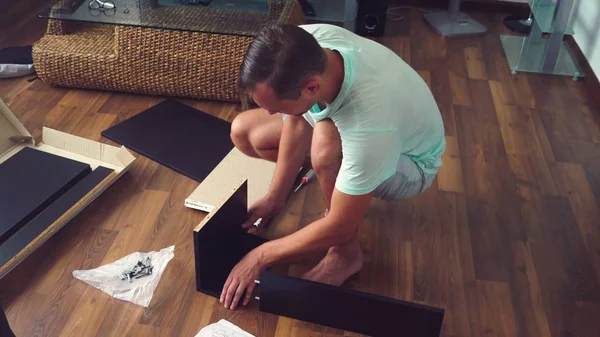 Ein junger Mann sammelt selbstständig Möbel im Wohnzimmer seines Hauses. Ein Mann sammelt einen Computertisch. — Stockfoto