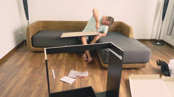 Egy fiatal férfi önállóan gyűjt bútor a nappaliban a házból. Az ember gyűjt a számítógép asztal. — Stock Fotó