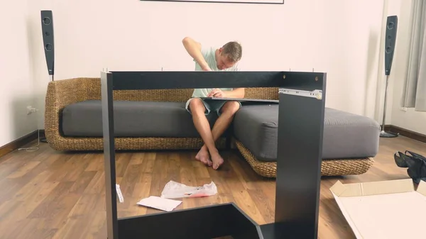 Ένας νεαρός άνδρας συλλέγει ανεξάρτητα επίπλων στο σαλόνι του σπιτιού του. Ένας άνθρωπος συλλέγει ένα γραφείο υπολογιστή. — Φωτογραφία Αρχείου