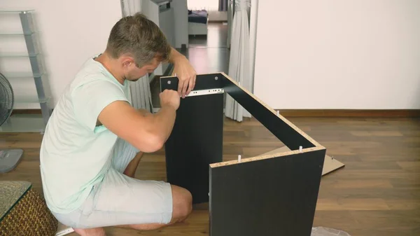 Seorang pemuda secara independen mengumpulkan perabotan di ruang tamu rumahnya. Seorang pria mengumpulkan meja komputer . — Stok Foto