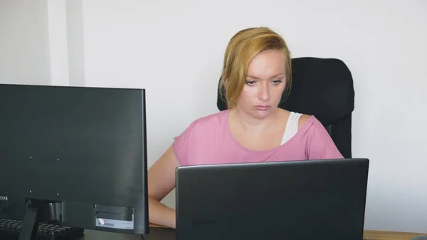 Hermosa mujer joven que trabaja en un ordenador portátil y un ordenador mientras está sentado en un escritorio . —  Fotos de Stock