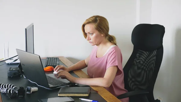 Hermosa mujer joven que trabaja en un ordenador portátil y un ordenador mientras está sentado en un escritorio . — Foto de Stock