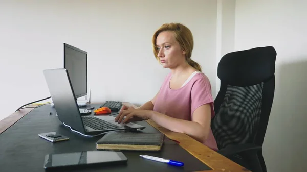 Bela jovem mulher trabalhando em um laptop e computador enquanto sentado em uma mesa . — Fotografia de Stock
