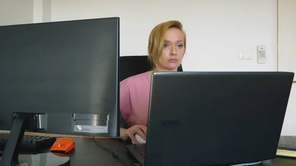 Belle jeune femme travaillant sur un ordinateur portable et un ordinateur tout en étant assis à un bureau . — Photo