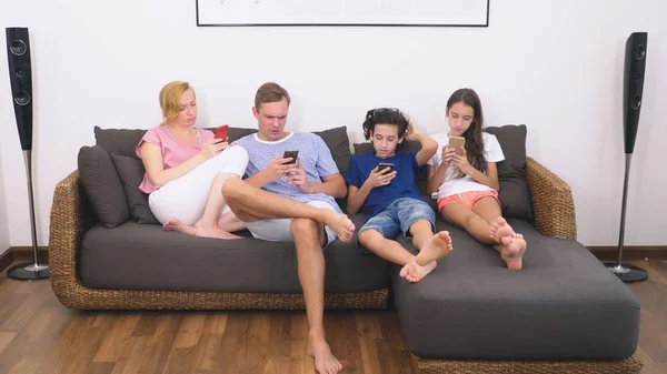 Familia encantadora, mamá, papá, hija e hijo están viendo la televisión en la sala de estar juntos, todo el mundo está mirando en su teléfono — Foto de Stock
