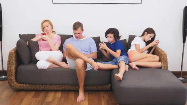 Чарівна сім'я, мама, тато, дочка і син дивляться телевізор у вітальні разом, всі дивляться в його телефон — стокове фото