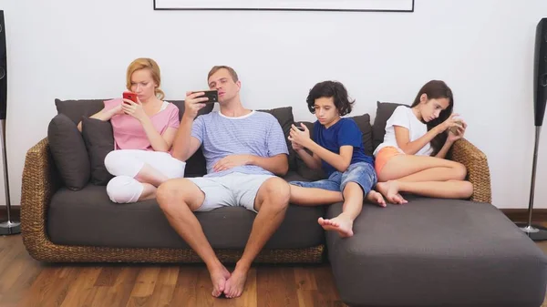Чарівна сім'я, мама, тато, дочка і син дивляться телевізор у вітальні разом, всі дивляться в його телефон — стокове фото
