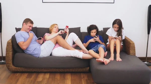 Familia encantadora, mamá, papá, hija e hijo están viendo la televisión en la sala de estar juntos, todo el mundo está mirando en su teléfono — Foto de Stock