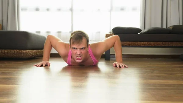Playful handsome guy in a pink t-shirt engaged in fitness, in the living room of his house.