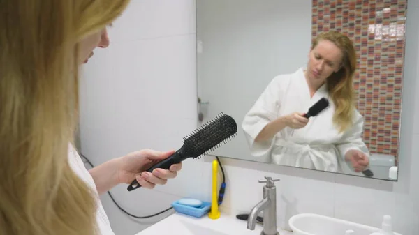 Haar gezondheid, haar verlies concept. Vrouw kammen van haar blond beschadigd droge haren in de badkamer — Stockfoto