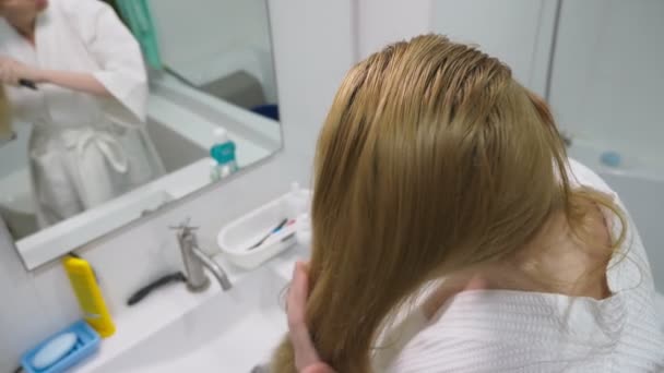 Salute dei capelli, concetto di perdita dei capelli. Donna pettinando i suoi capelli biondi danneggiati secchi in bagno — Video Stock