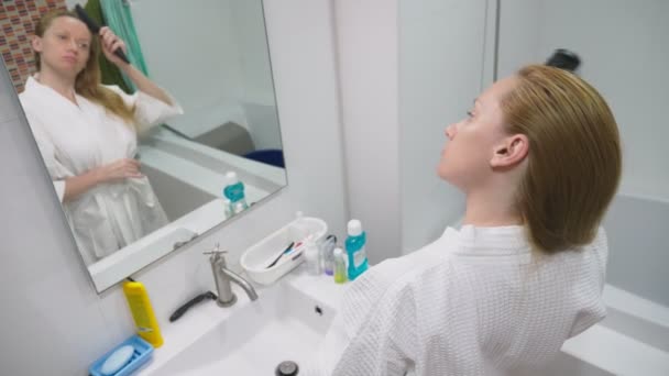 Salud del cabello, concepto de pérdida de cabello. Mujer peinando su cabello rubio seco dañado en el baño — Vídeo de stock