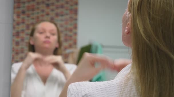 Концепция ухода за лицом. Женщина наносит косметический лосьон для ухода за кожей в ванной комнате. Утренняя гигиена — стоковое видео