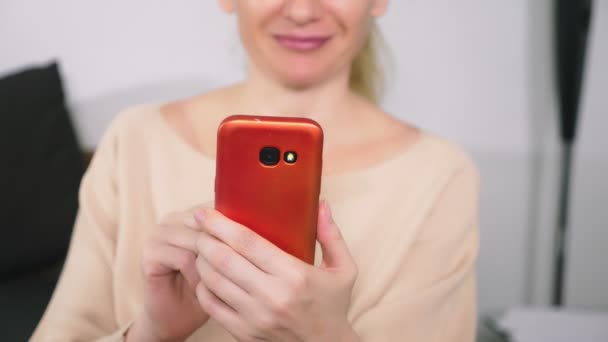 Hermosa chica utilizar un teléfono inteligente celular mientras está sentado en la sala de estar por la noche. Feliz sonriente joven mujer charlando en internet en casa . — Vídeos de Stock