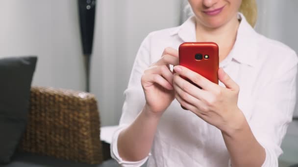 Mooi meisje een cellulaire smartphone gebruiken tijdens de vergadering in de woonkamer in de avond. Gelukkig lachende jonge vrouw chatten op het internet thuis. — Stockvideo