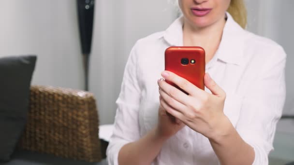 Beautiful girl use a cellular smartphone while sitting in the living room in the evening. Happy smiling young woman chatting on the internet at home. — Stock Video