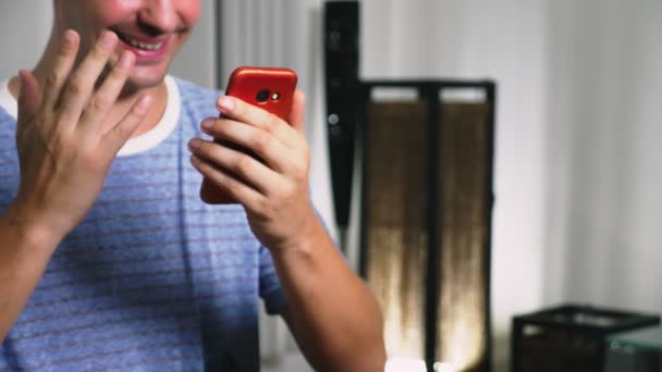 Hermoso gay utilizar un teléfono inteligente celular mientras está sentado en la sala de estar por la noche. Feliz joven sonriente charlando en Internet en casa . — Vídeos de Stock